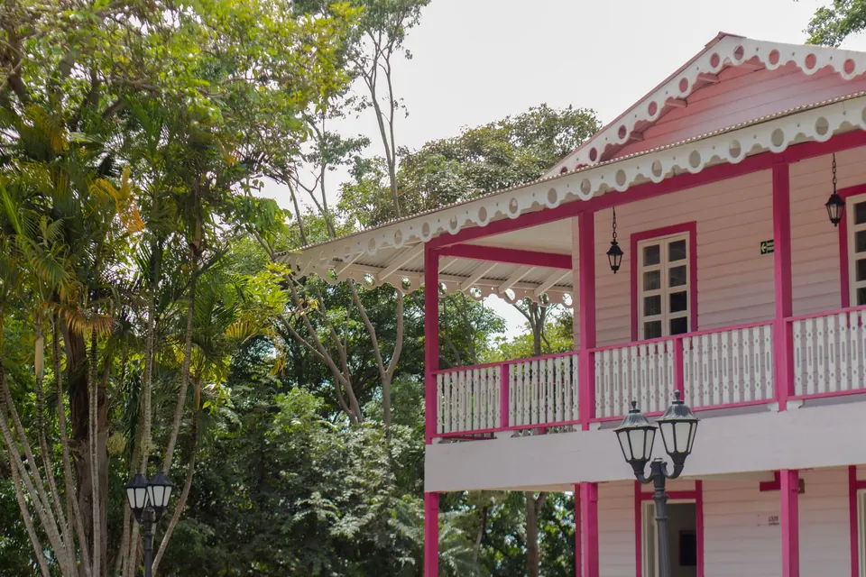 Maison en bois rose et blanc à balcon ouvragé, au milieu de la verdure