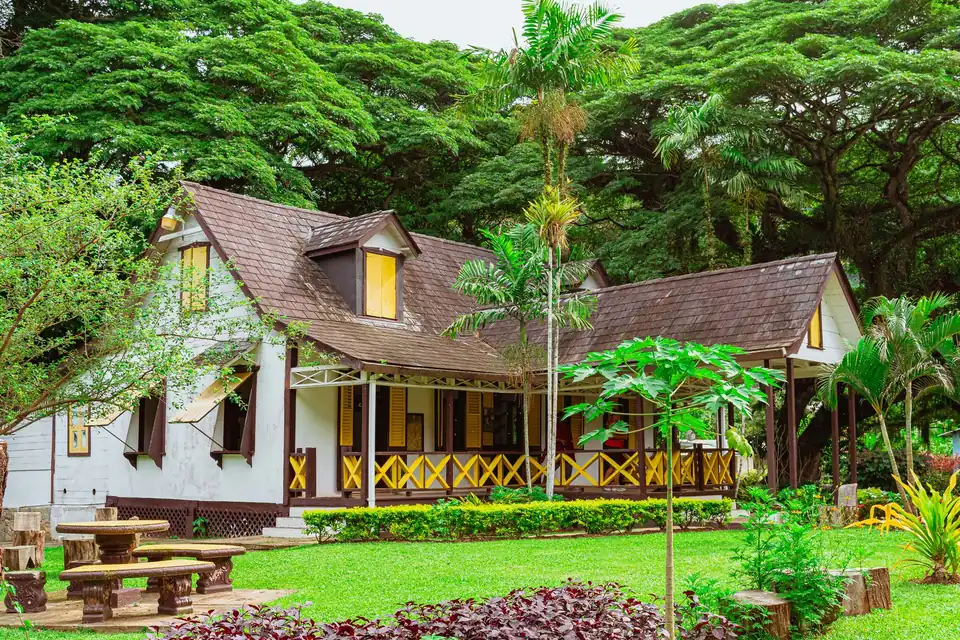Maison en bois à véranda et lucarnes, entourée d'un jardin tropical