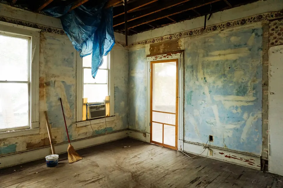 Pièce d'une maison ancienne en travaux, murs écaillés, bâche et outils au sol