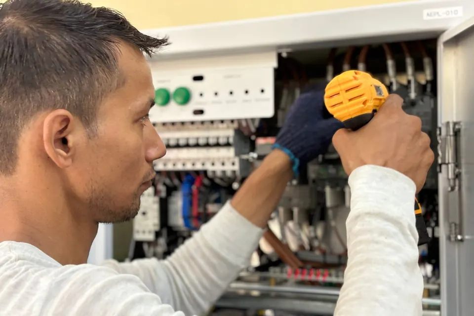 Technicien intervenant à la visseuse sur un tableau électrique